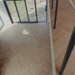 Jasna podłoga winylowa układana w wzór jodełki w nowoczesnym wnętrzu z dużymi przeszkleniami.