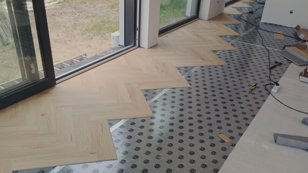 Układanie jasnej podłogi winylowej w jodełkę, narzędzia instalacyjne na podłodze przy otwartym oknie